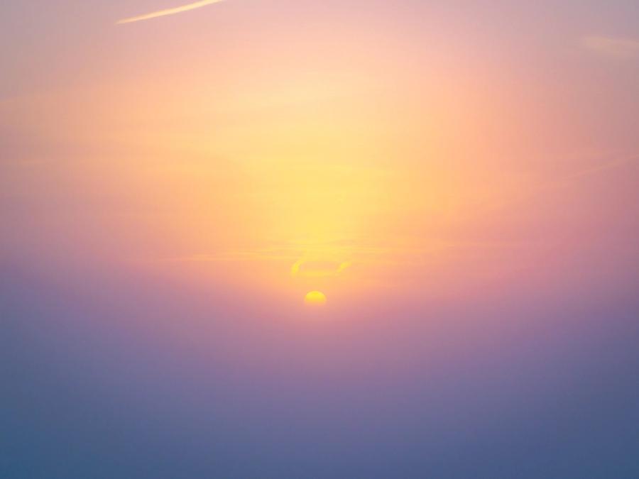 The setting sun drops beneath a thin band of cloud above the Thames Valley, its disc diffused by haze into a soft corona of amber and mauve. Captured by drone near Abingdon-on-Thames in early March, the image records a moment of atmospheric optical separation rather than a conventional sunset composition.