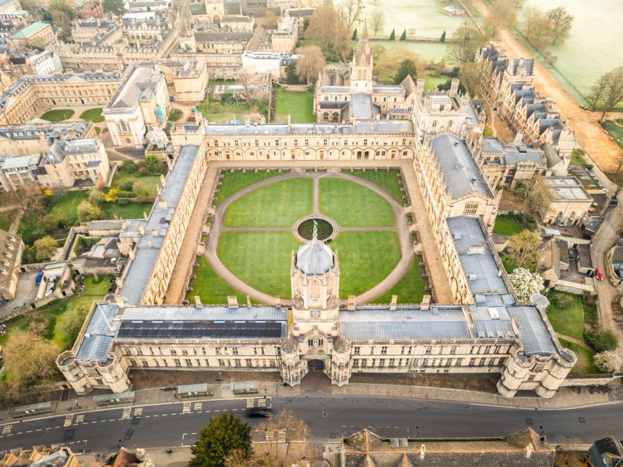 The symmetrical courtyard of Christchurch College, resolves from directly overhead into a geometry of limestone colonnades and circular lawn paths centred on a small fountain. Shot in flat spring light on 22 March, the overcast sky strips the scene of shadow drama but renders the Cotswold stone evenly, emphasising pattern over atmosphere. The image is competent and well-framed but reads as architectural documentation rather than a distinctive aerial landscape.