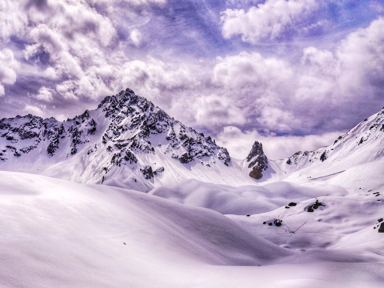 Heavy snowfall covered the three valleys in over a metre of snow late in the ski season across the French Alps in Courcheval. It smoothed out the rolling rocky landscape into undulating white mounds, right towards the jagged peaks of these huge mountains. Low clouds rolled over the peaks, almost like candy floss. You can see marmotte trails in the snow, having emerged from their winter hibernation.