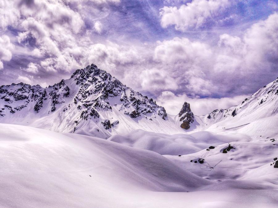 Heavy snowfall covered the three valleys in over a metre of snow late in the ski season across the French Alps in Courcheval. It smoothed out the rolling rocky landscape into undulating white mounds, right towards the jagged peaks of these huge mountains. Low clouds rolled over the peaks, almost like candy floss. You can see marmotte trails in the snow, having emerged from their winter hibernation.