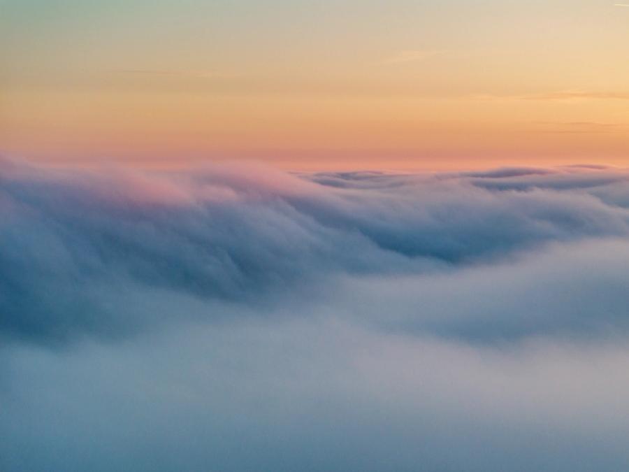 A temperature inversion buries the Thames Valley beneath a rolling sea of low cloud near Abingdon-on-Thames, the upper surface catching the last warm tones of a March sunset. Striations across the cloud top suggest gentle airflow, giving the otherwise featureless mass a quiet structural rhythm. The gradient from cool blue below to peach and teal at the horizon holds the eye without a conventional anchor point.