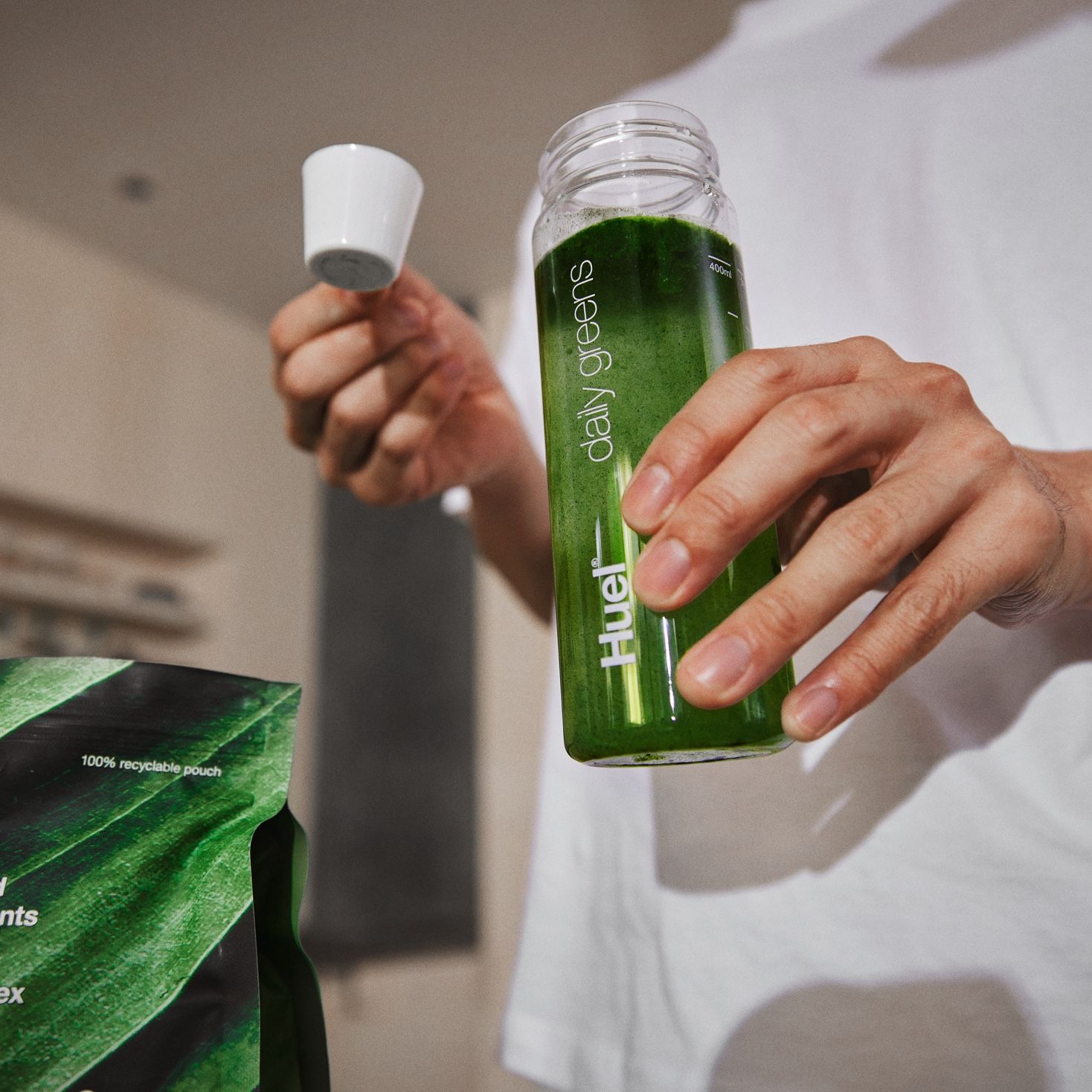Person in a kitchen filling a Huel Daily Greens Bottle with Huel Daily Greens Powder