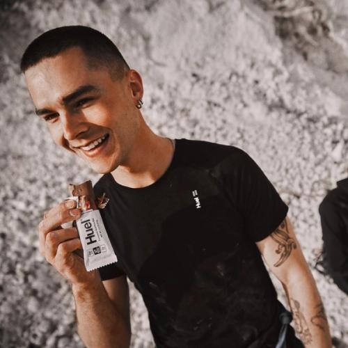 A smiling man eating a Huel protein bar against a rugged mountainous background