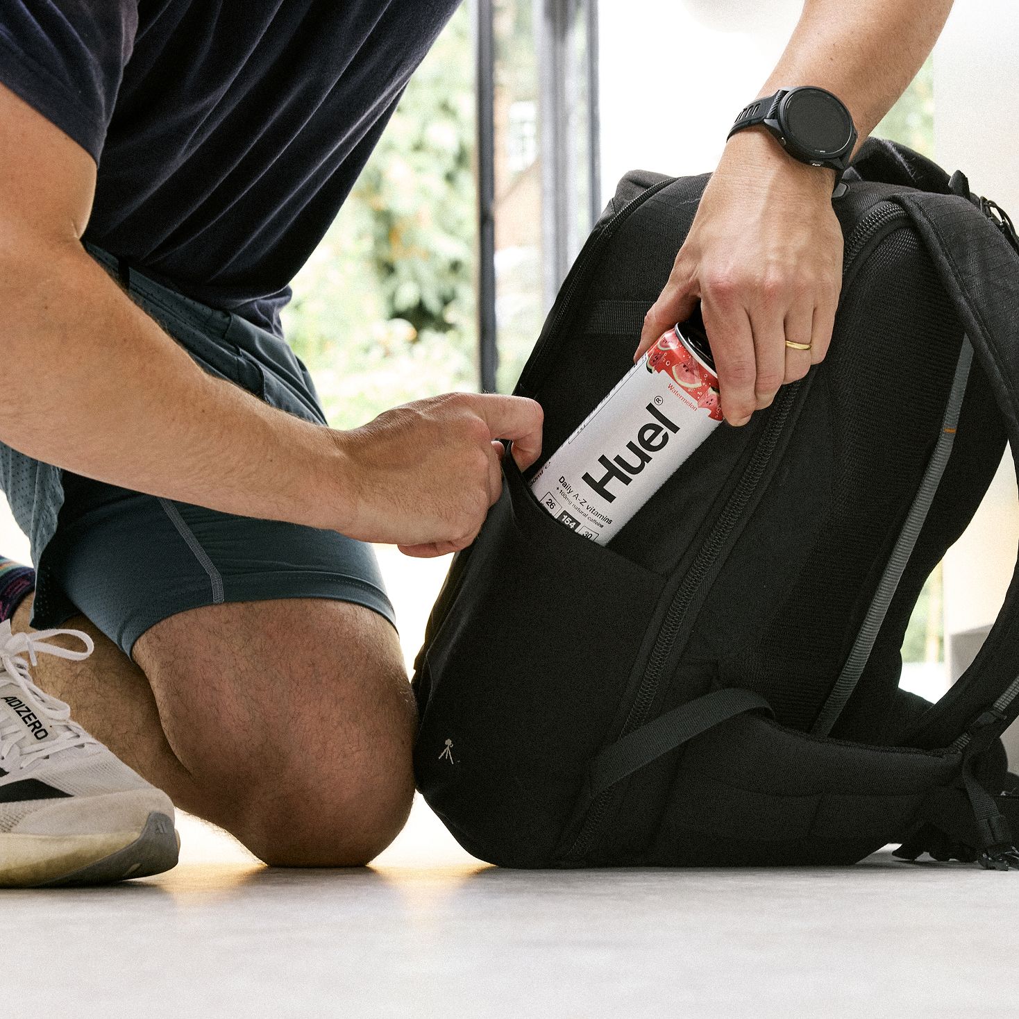 A man pulling a watermelon Huel Daily-A-Z vitamins out of the side of a black backpack