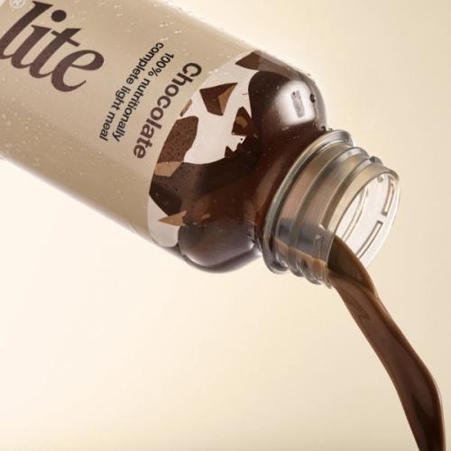 Huel chocolate pouring from a bottle of Huel Ready-to-drink lite on a beige background