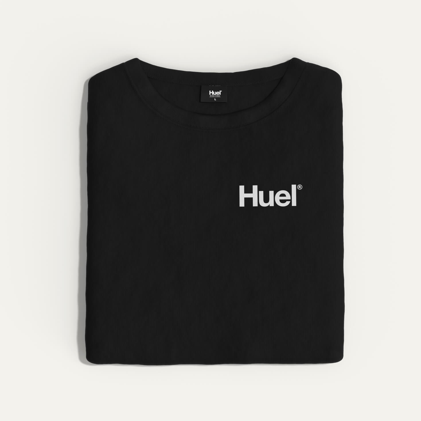 A folded black Huel t-shirt with a white 'Huel' logo on it, resting on a neutral surface