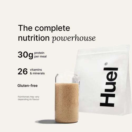 A bag of Huel powder next to a glass containing a Huel drink on a neutral background