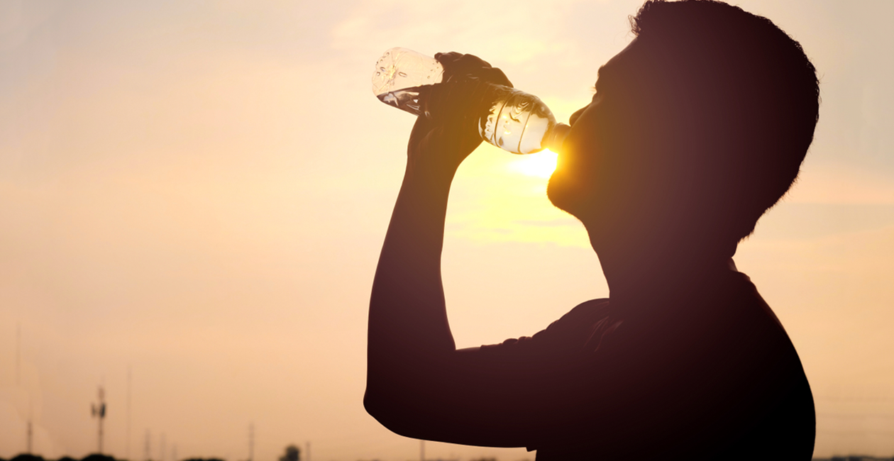 A silhouette of a man drinking a bottle of water with a sunset background