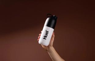 Someone holding a Huel shaker on a brown background