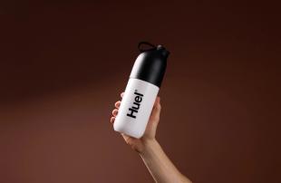 Someone holding a Huel shaker on a brown background