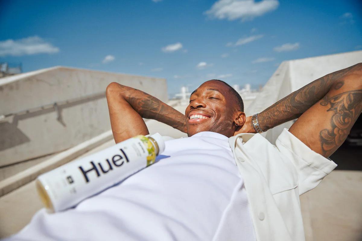 man laying in the sun smiling with a huel ready to drink resting on his chest