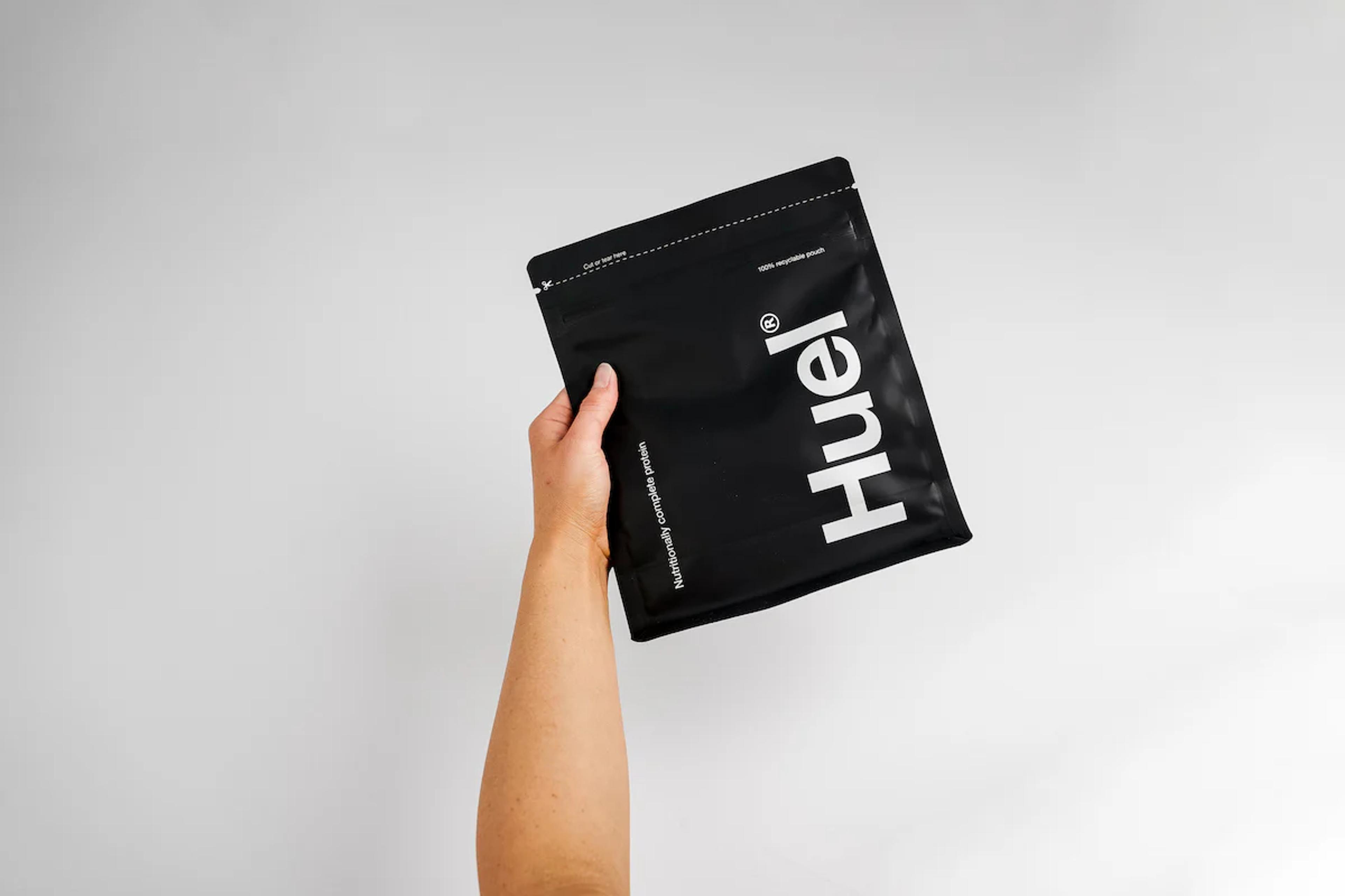 Hand holding a pouch of Huel Black Edition Powder with a white background