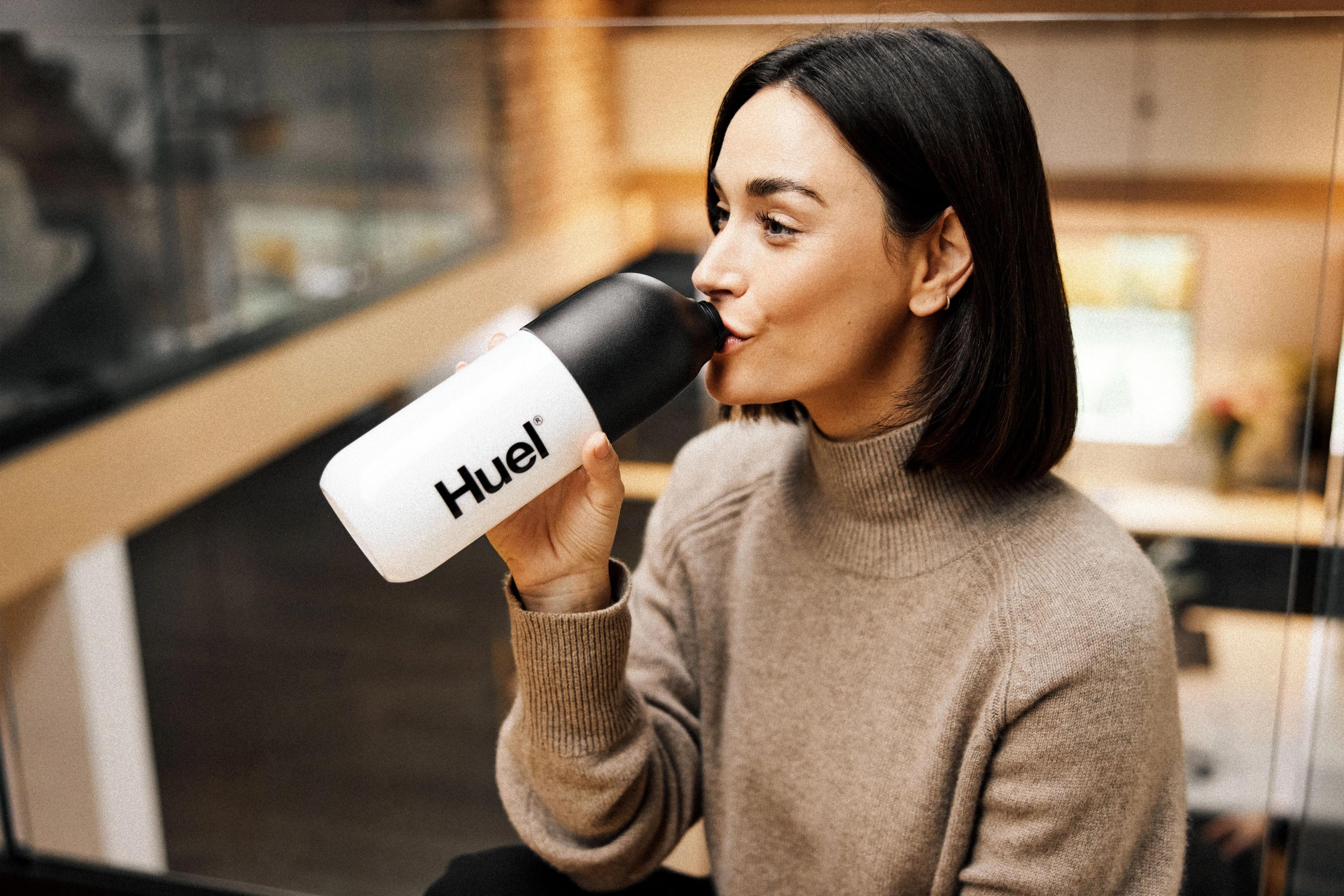 Woman drinking from a Huel shaker inside