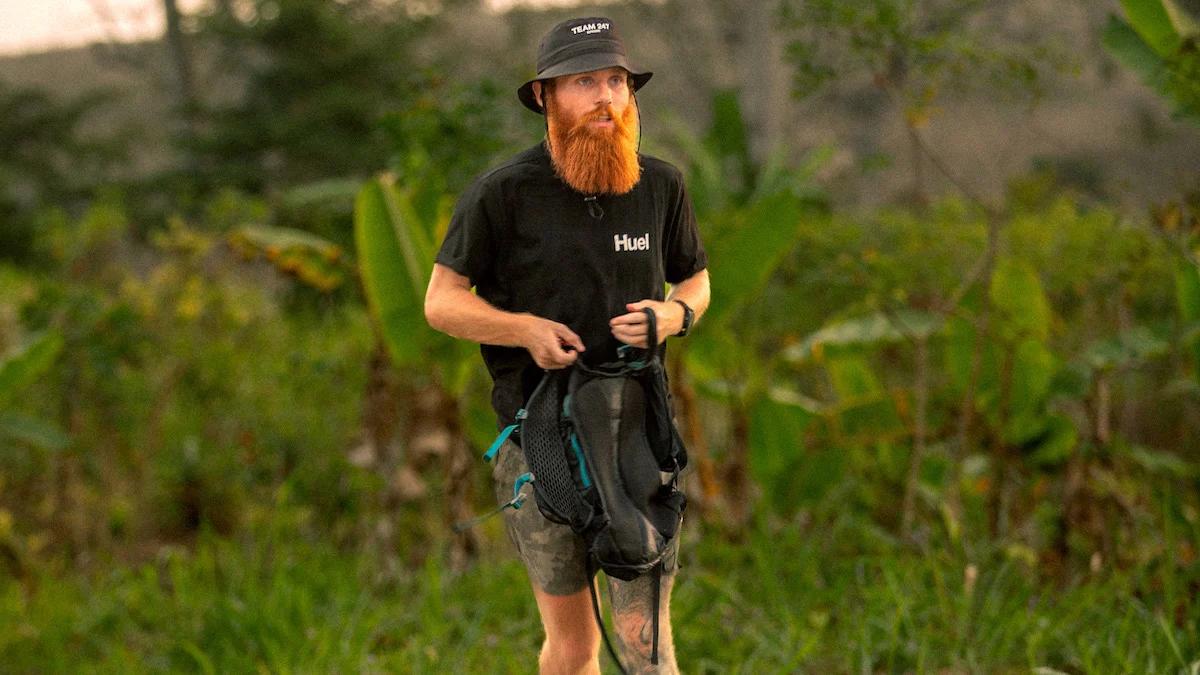 Russ Cook stood in nature wearing a bucket hat and huel tshirt