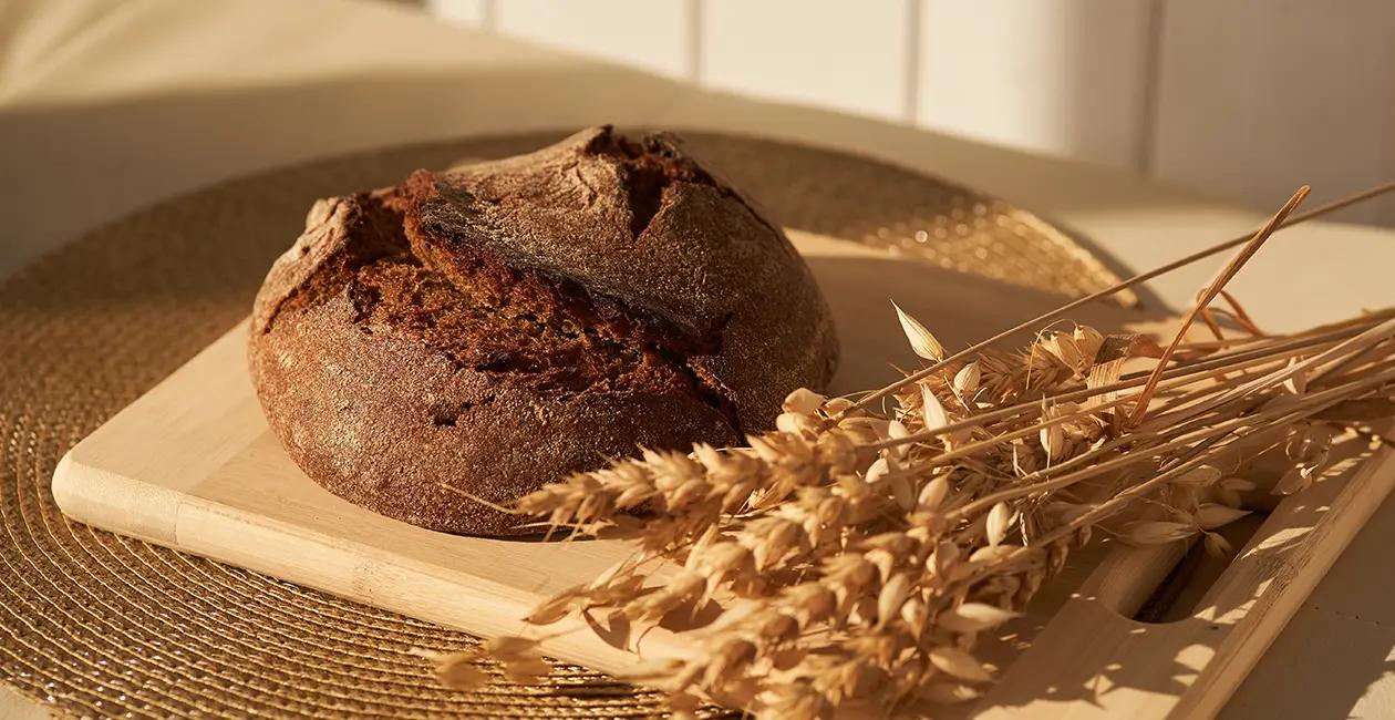 a freshly baked loaf of bread on a wooden board next to some raw wheat