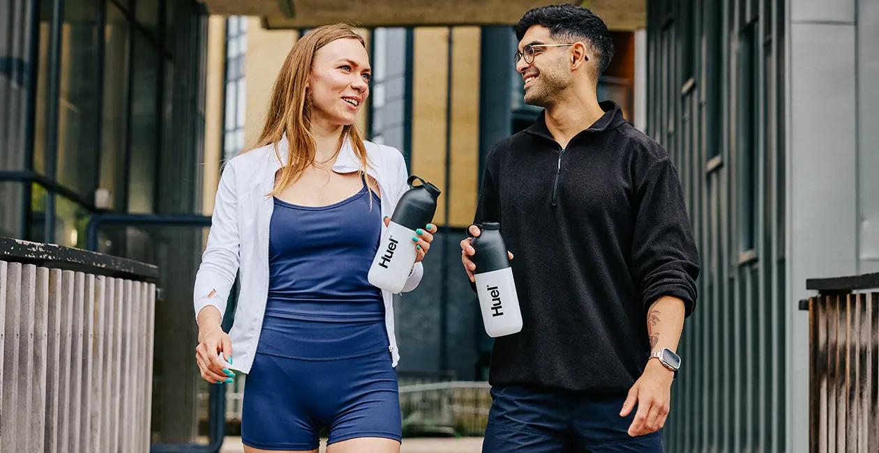 man and woman walking along chatting and holding Huel shakers