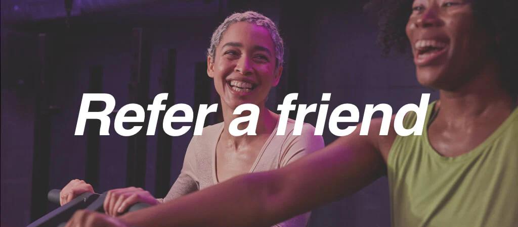 Two women having fun when working out in the gym with 'Refer-a-friend' text overlayed onto the image