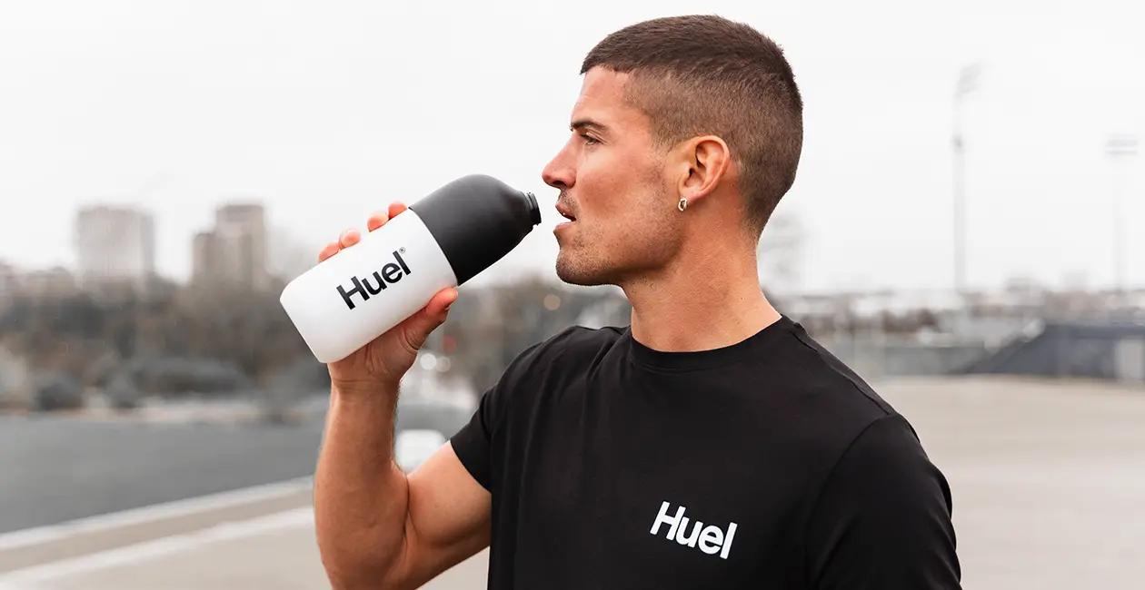man stood outside wearing a Huel tshirt and drinking from a Huel shaker