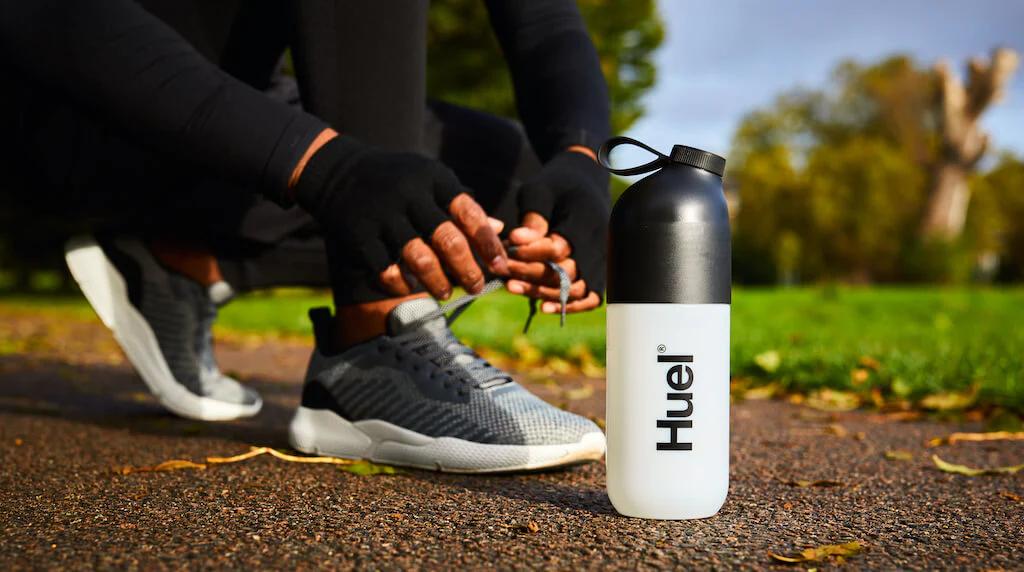 Man tying his trainers in a park ready to run, while next to a Huel shaker.