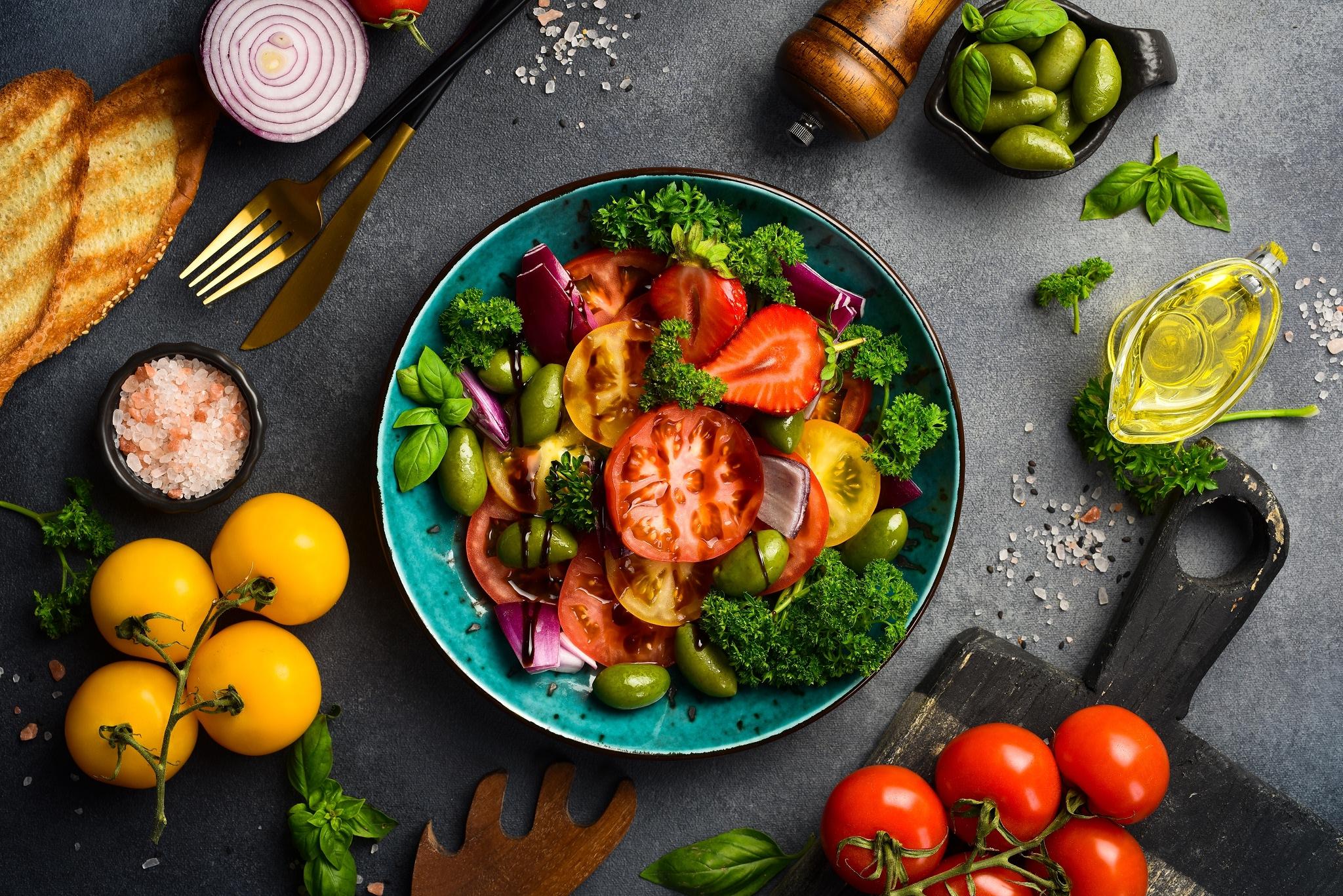 Bowl full of salad with other ingredients around it from a birds eye view