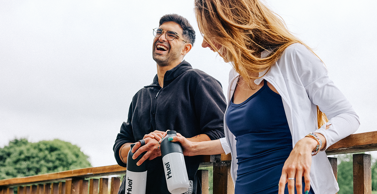 man and woman stood outside leaning on a wooden railing laughing