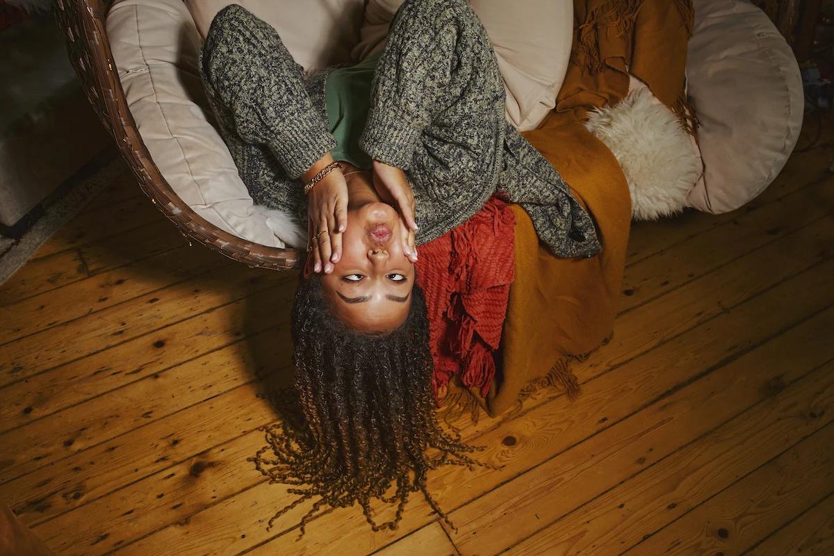 woman laying with her head over the edge of a sofa with her hands on her cheeks pulling a funny face