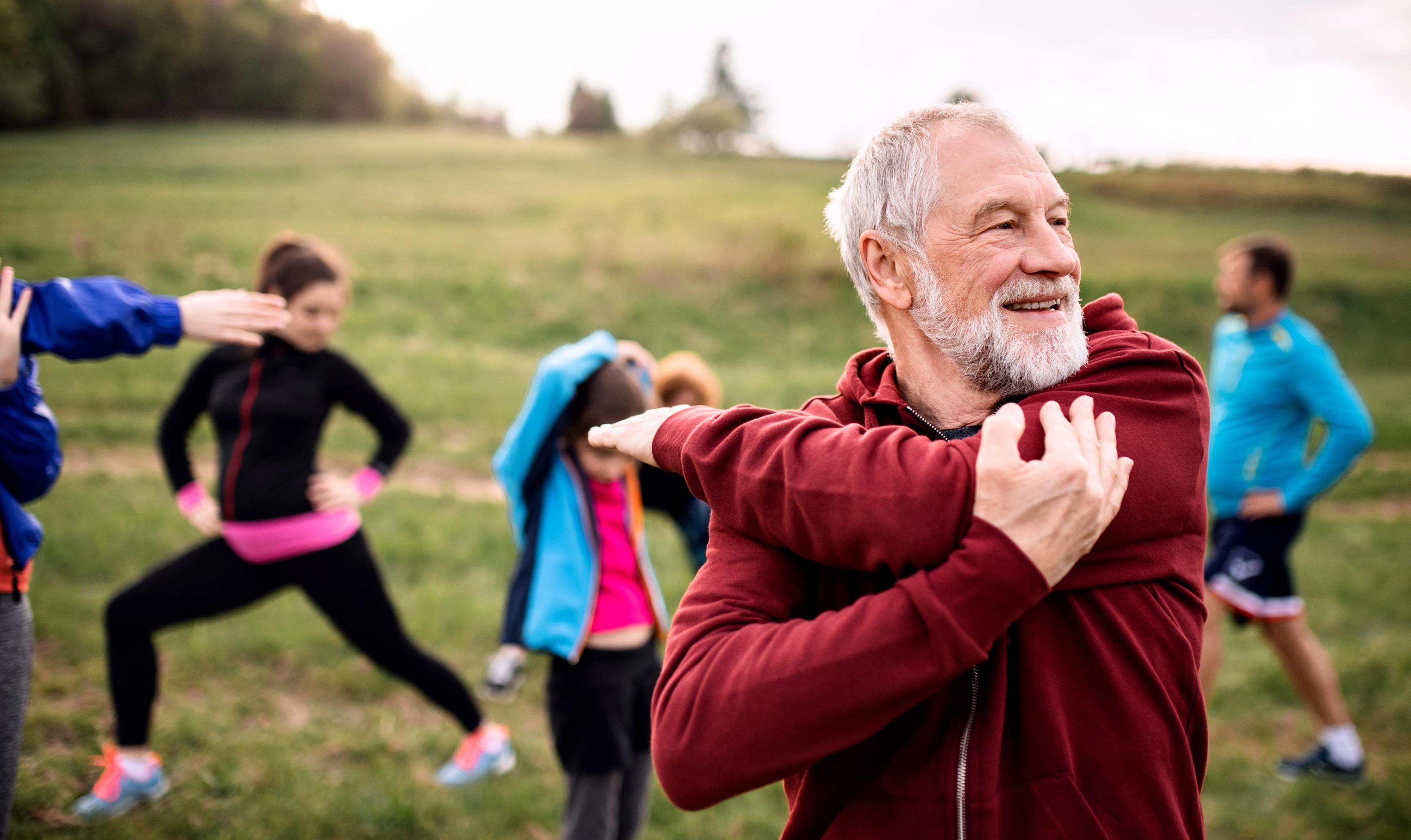 man outside stretching his arm across his chest with other people stretching in the background