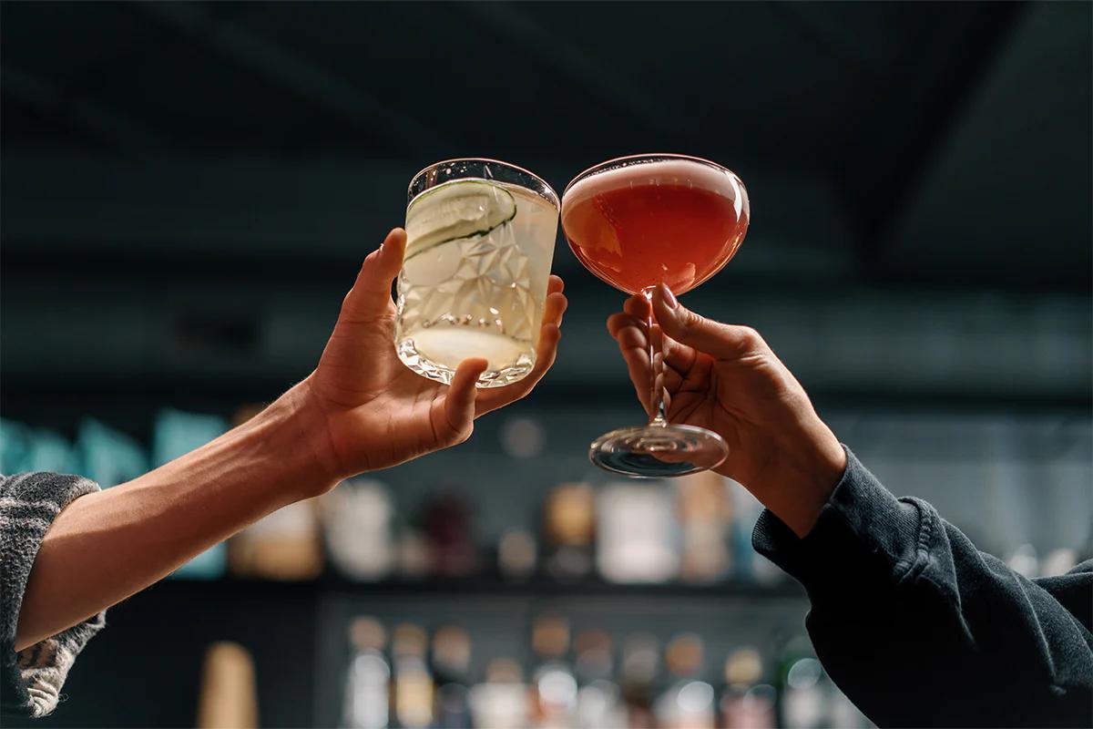 two people cheersing their cocktail glasses in a bar