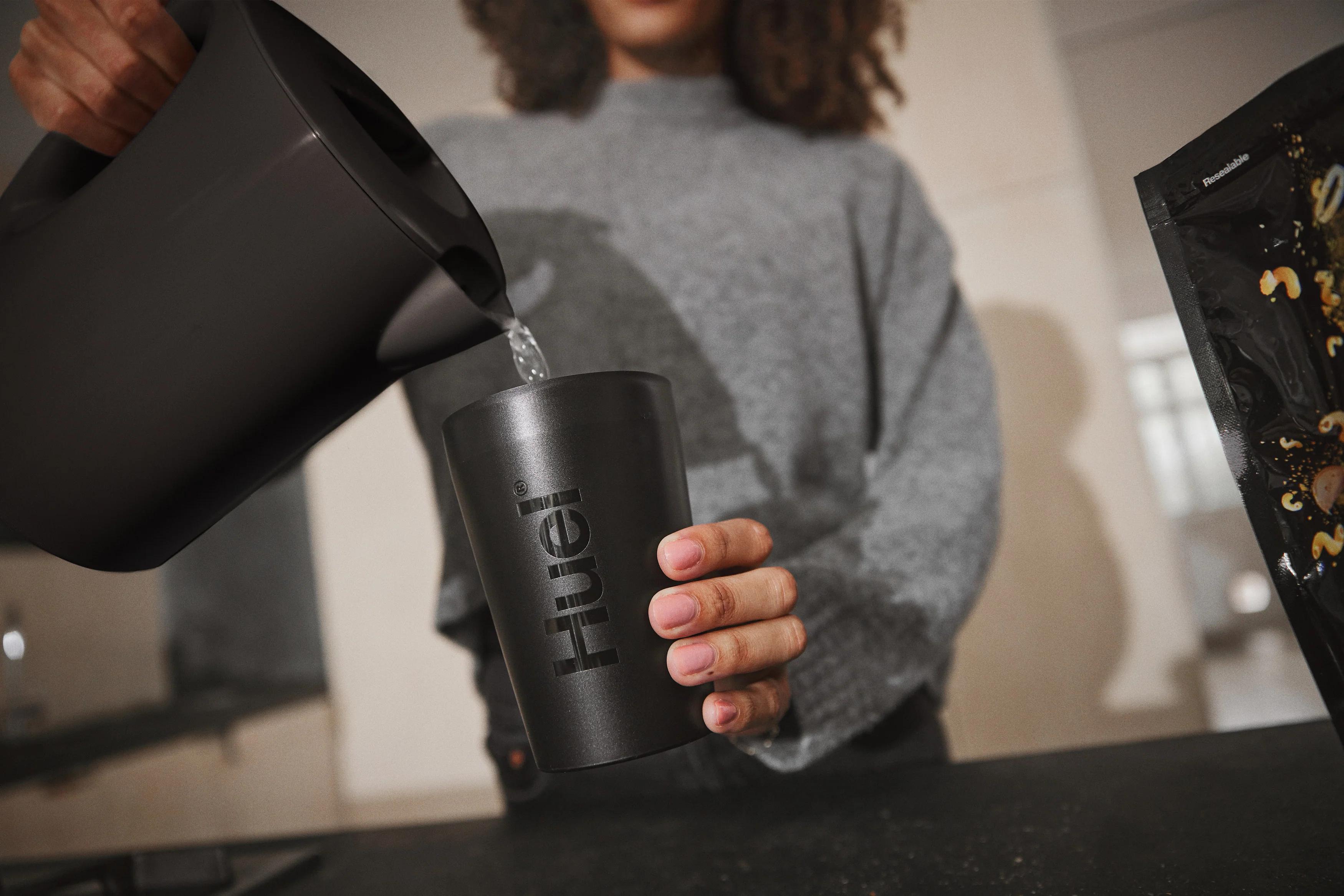 a woman pouring water from a kettle into a huel hot and savoury pot