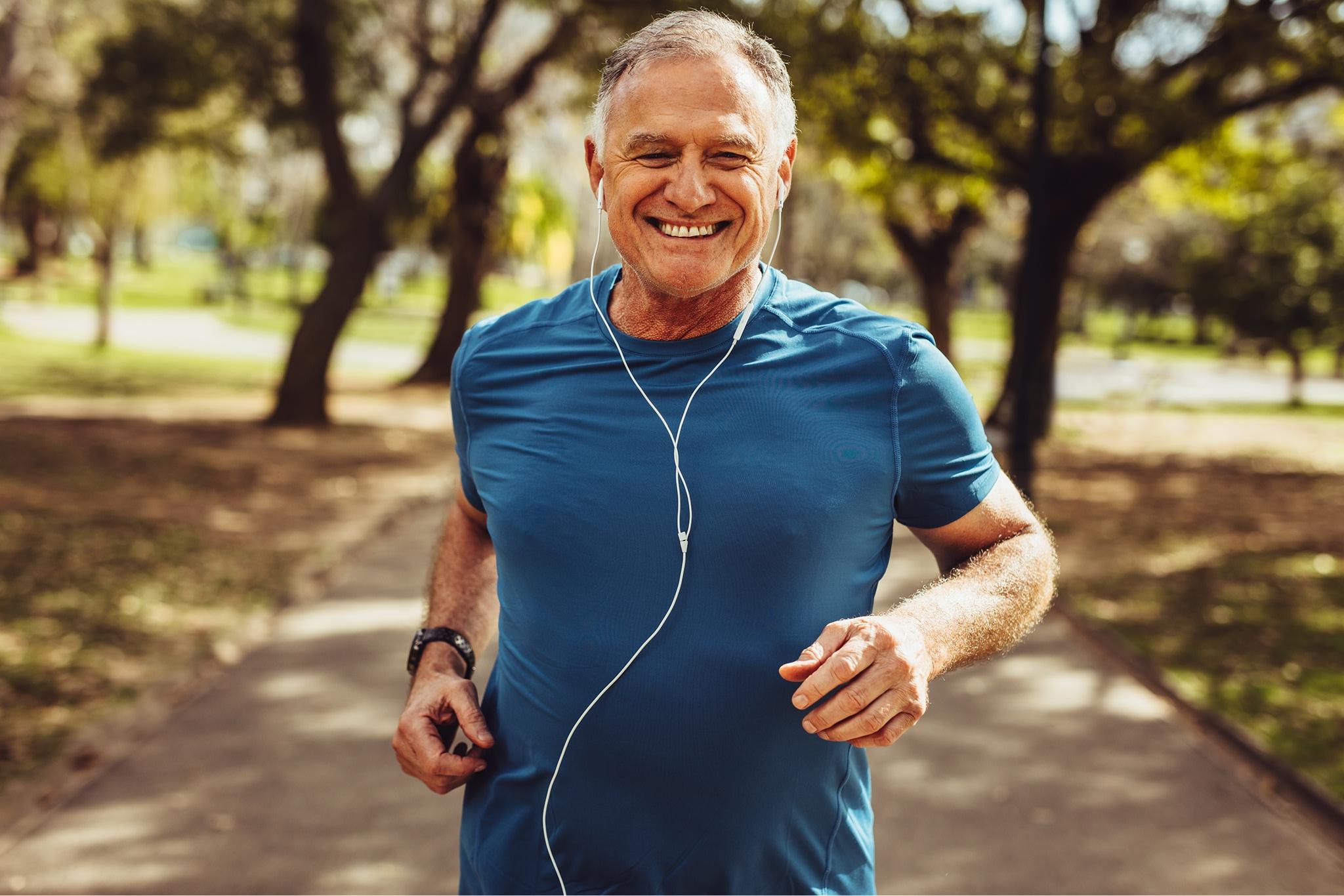 man jogging outside listening to music in his earphones while smiling