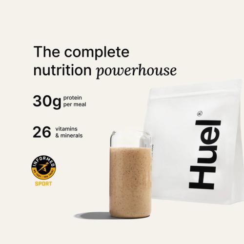 A bag of Huel powder next to a glass containing a Huel drink on a neutral background