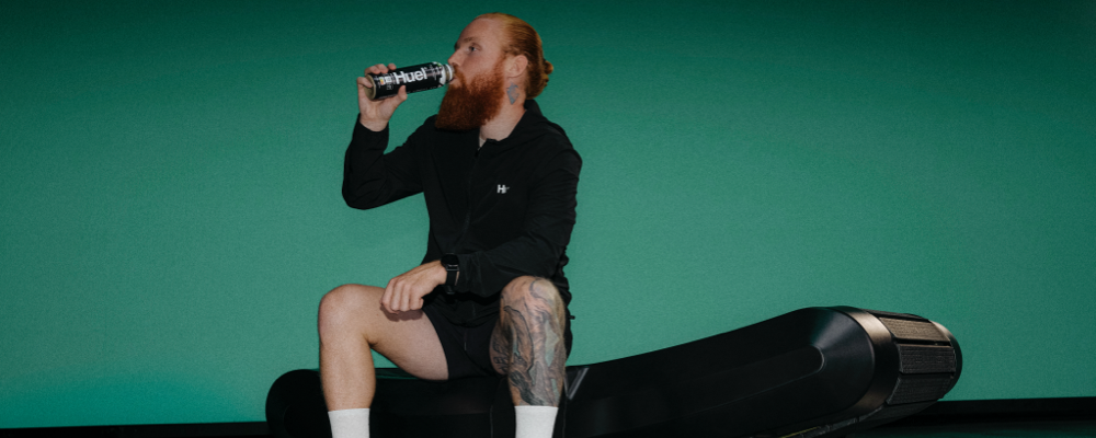 man sat on treadmill drinking from a bottle of Huel ready-to-drink