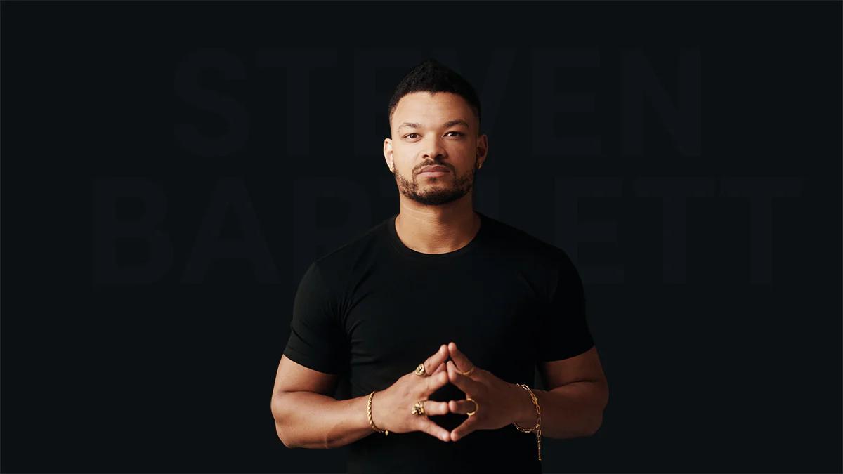 steven bartlett stood infront of a dark background with his hands together