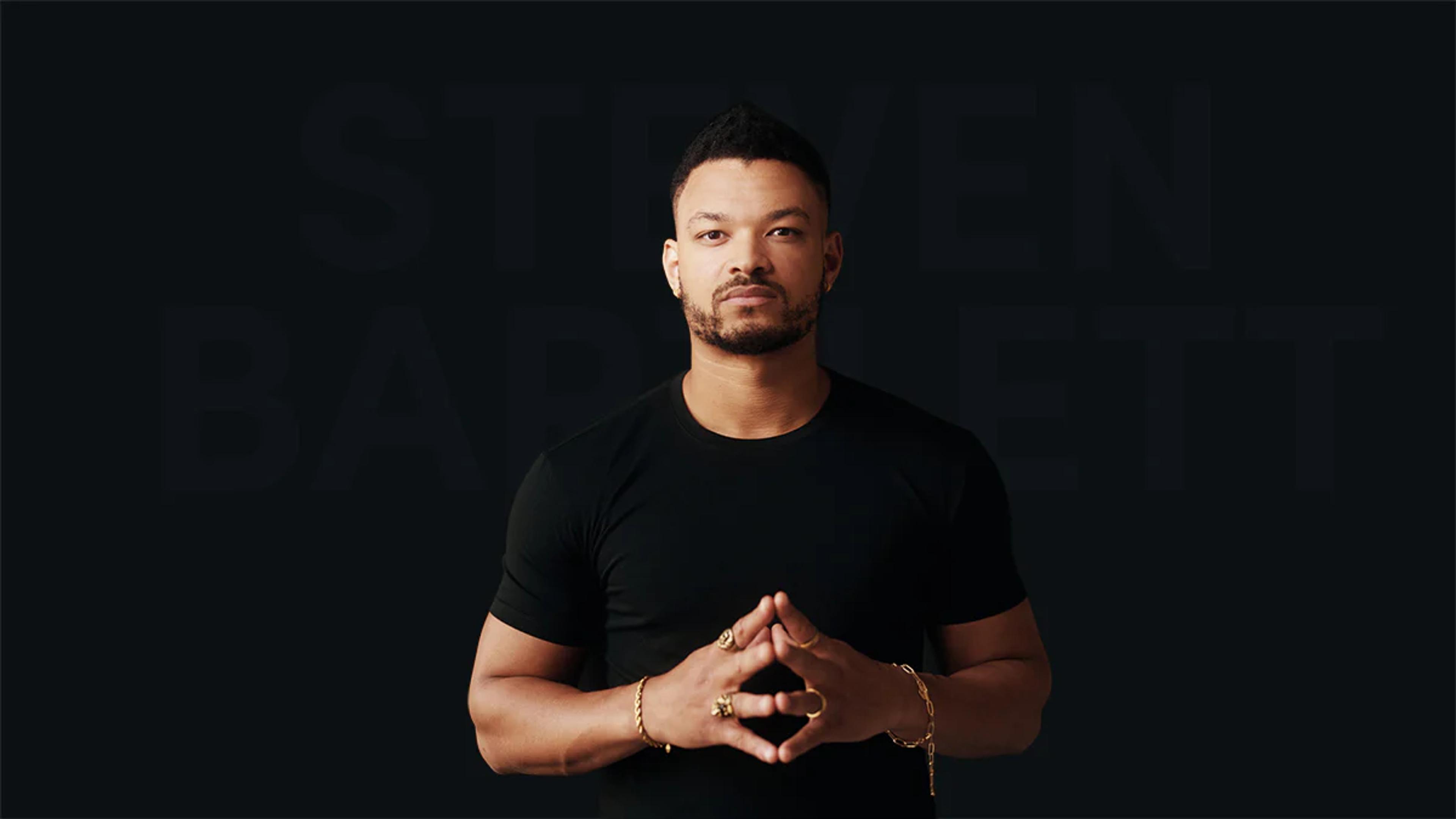 steven bartlett stood infront of a dark background with his hands together