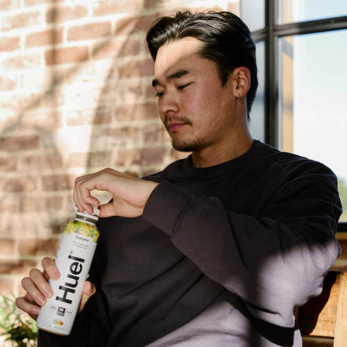 白い自転車用ヘルメットをかぶり、Huel Complete Nutritionのプロテインバーを食べる女性。