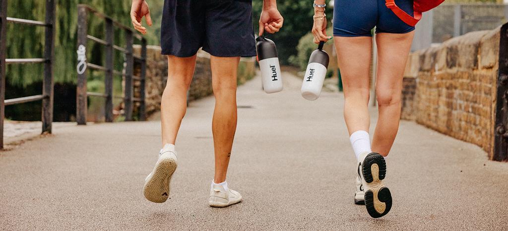 Man and women walking in trainers holding Huel shakers