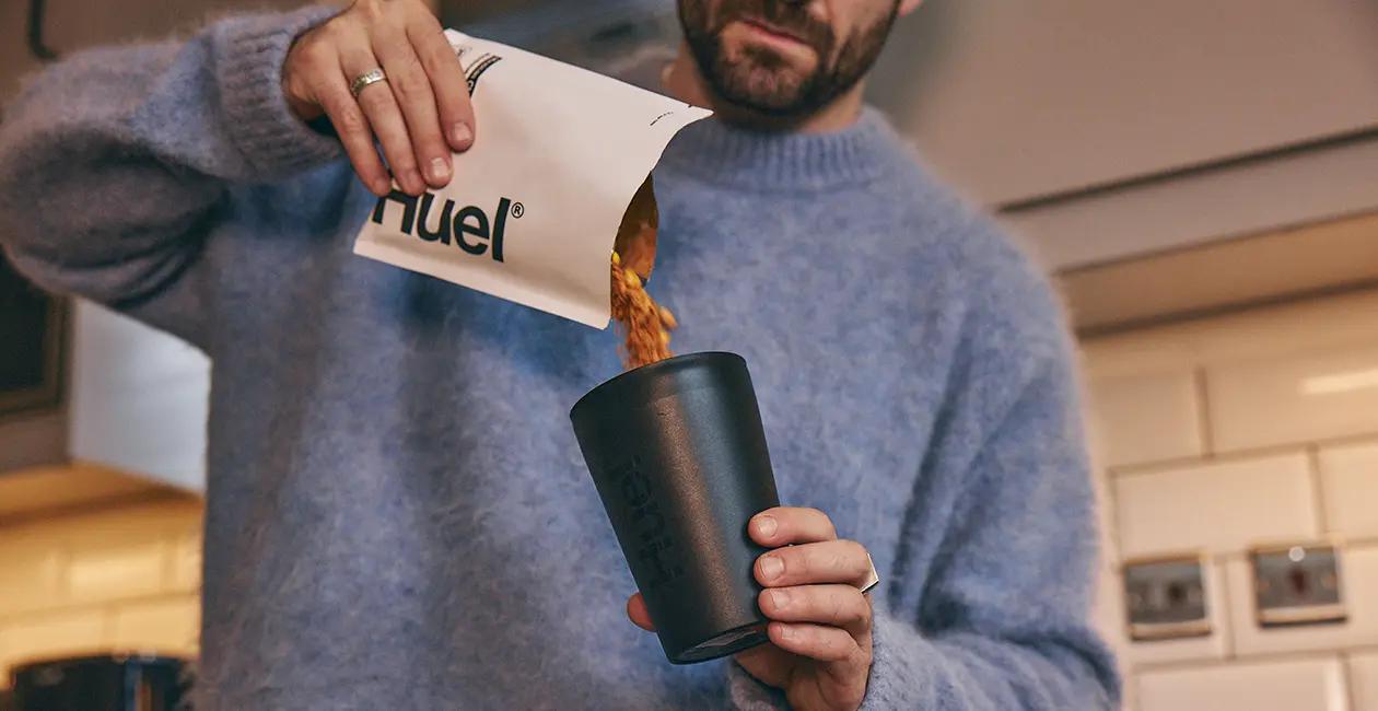 man pouring a Huel Hot & Savoury pack into a Huel Hot & Savoury pot