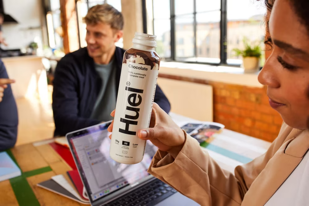 Woman holding a Huel Chocolate Ready-to-drink while sat at a table with other people