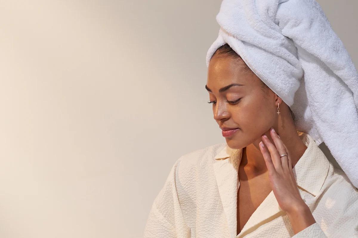 woman with her hair wrapped in a towel looking down and resting her fingers on her cheek