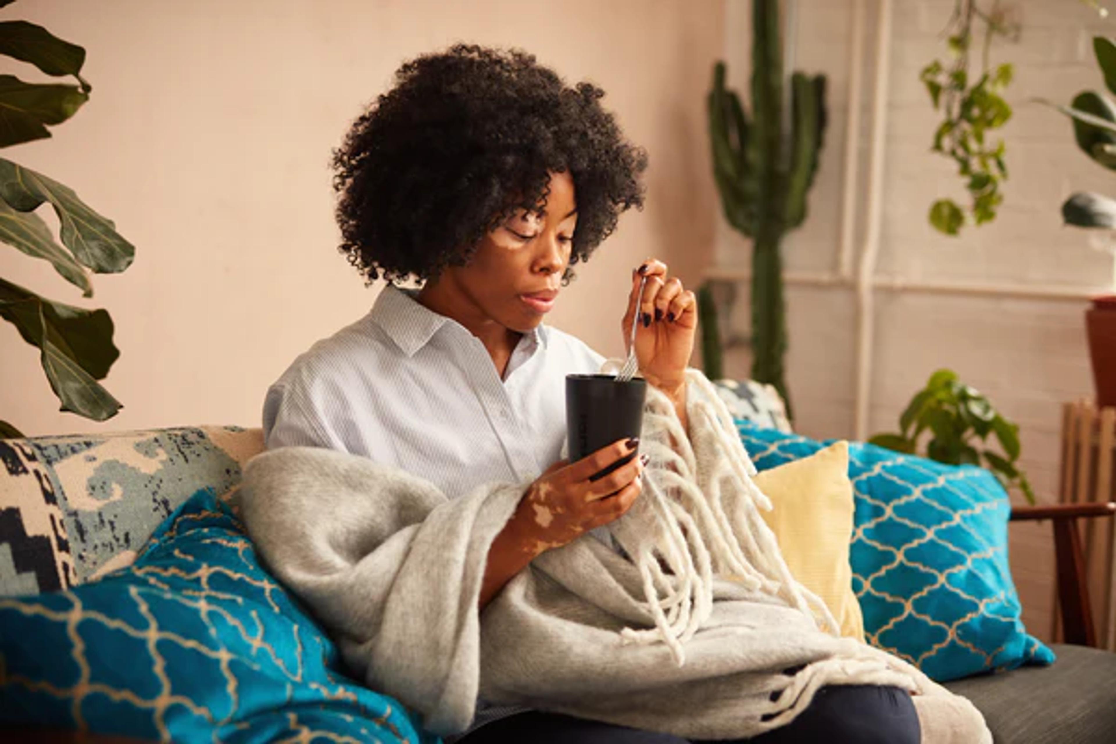 woman sat on sofa wrapped in a wool blanket eating Huel hot and savoury from a huel pot