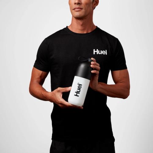 Marathon Runner Will Goodge wearing a black Huel t-shirt, drinking from a bottle of Huel Ready-to-drink