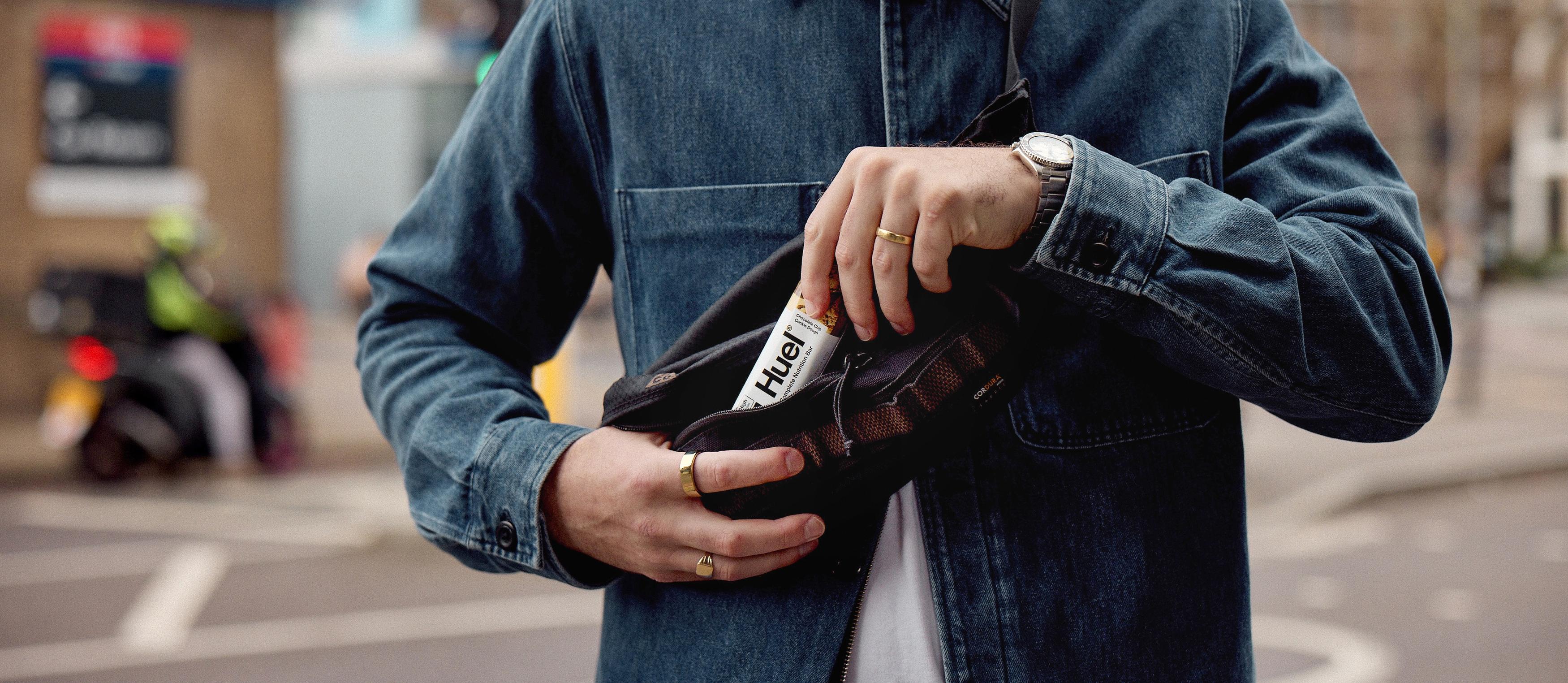 Man eating a chocolate Huel complete protein bar alongside a woman while on a hike
