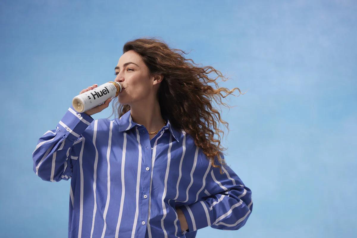 Woman wearing a purple and white striped shirt drinking a Huel Ready-to-drink