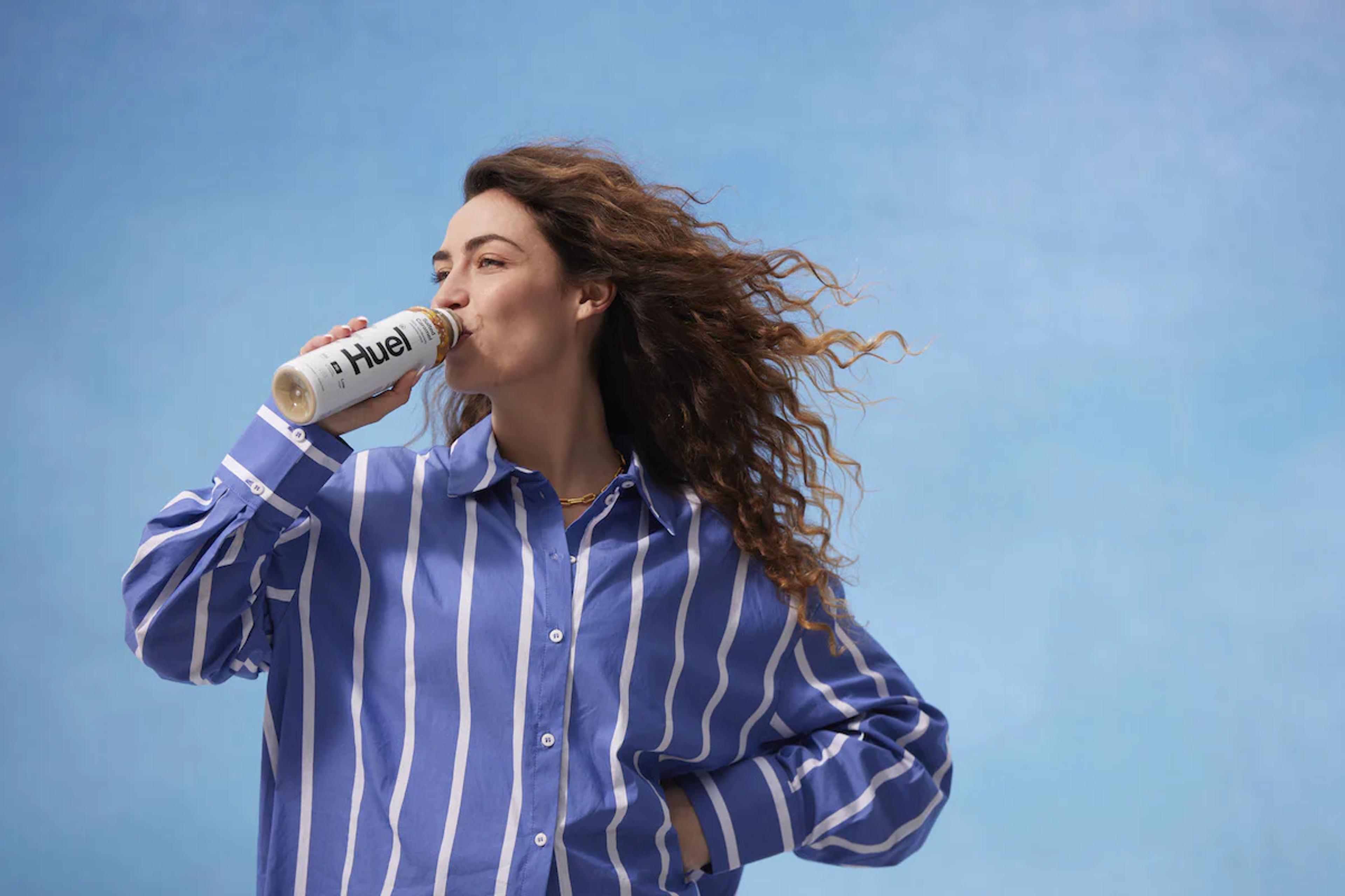 Woman wearing a purple and white striped shirt drinking a Huel Ready-to-drink