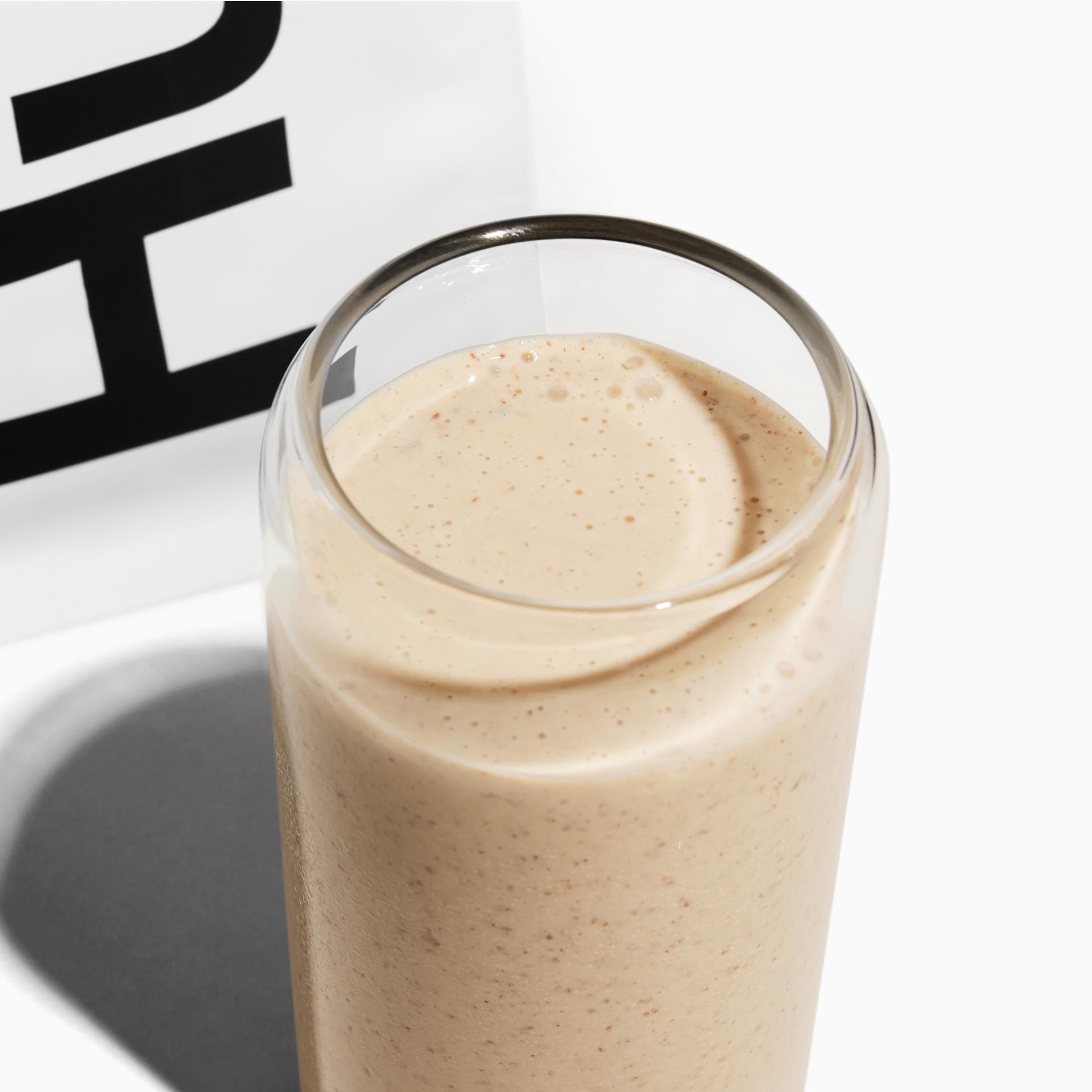 A glass of Huel shake next to a white bag of Huel Powder