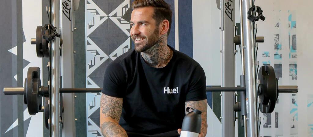 Man say on smith machine bench wearing Huel t-shirt and holding Huel shaker