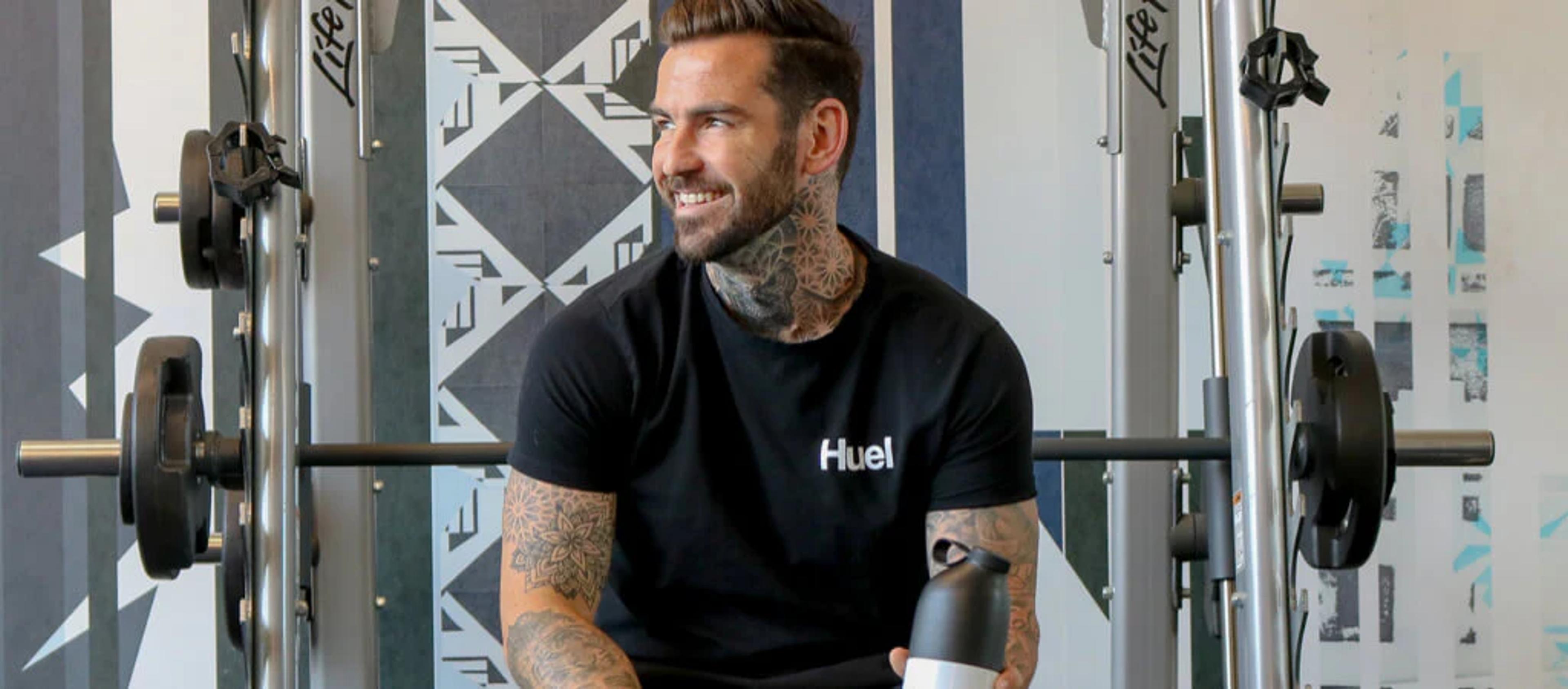 Man say on smith machine bench wearing Huel t-shirt and holding Huel shaker