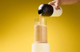 Someone pouring Huel Black Edition from a Huel shaker into a glass on a yellow background