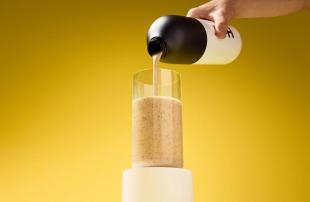 Someone pouring Huel Black Edition from a Huel shaker into a glass on a yellow background