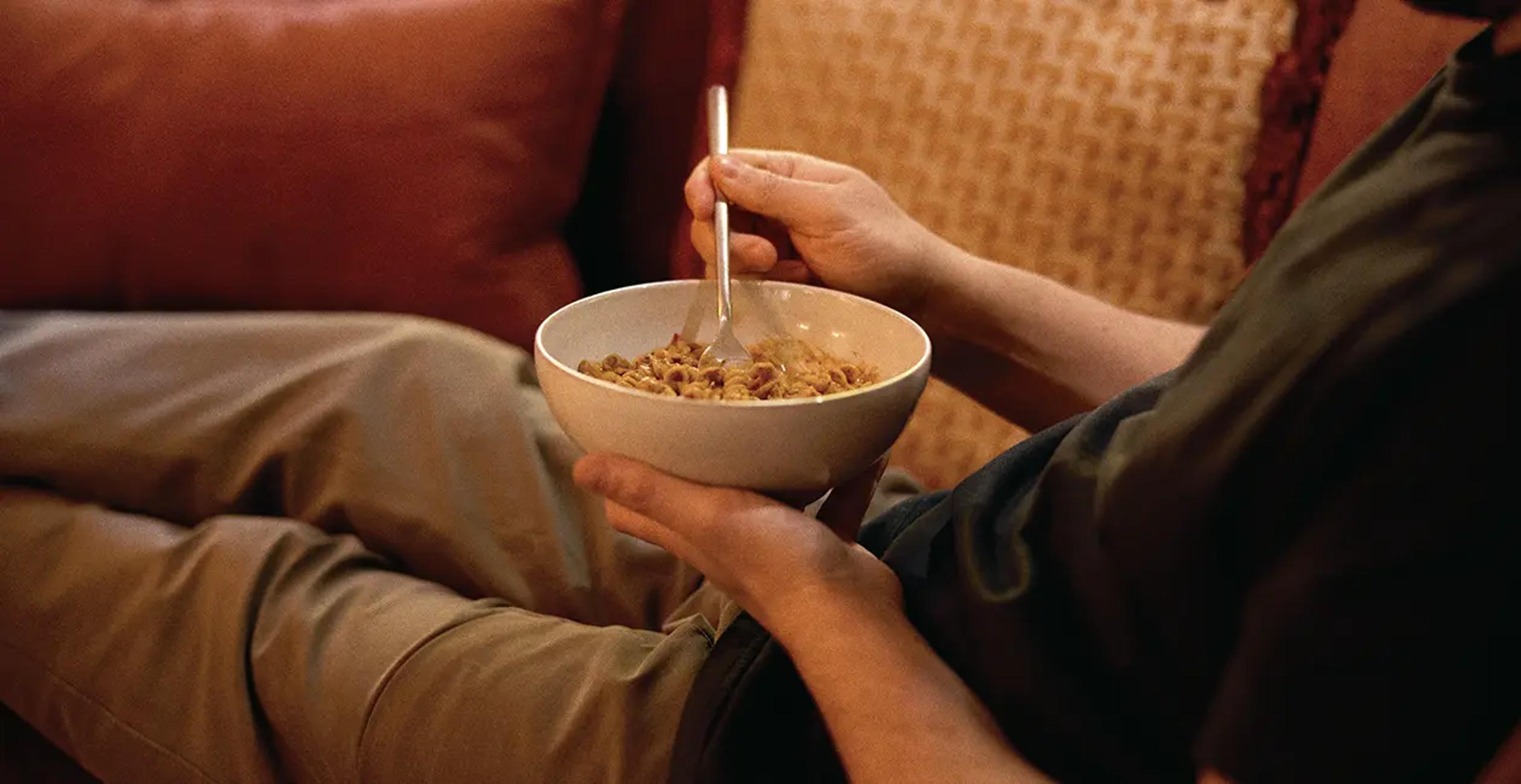 person eating Huel hot and savoury from a bowl while sat on the sofa with their feet up